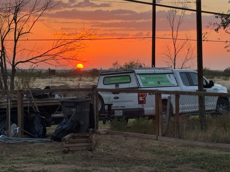 White pickup truck with camper bed parked at sunset behind a wooden fence with bare trees in background